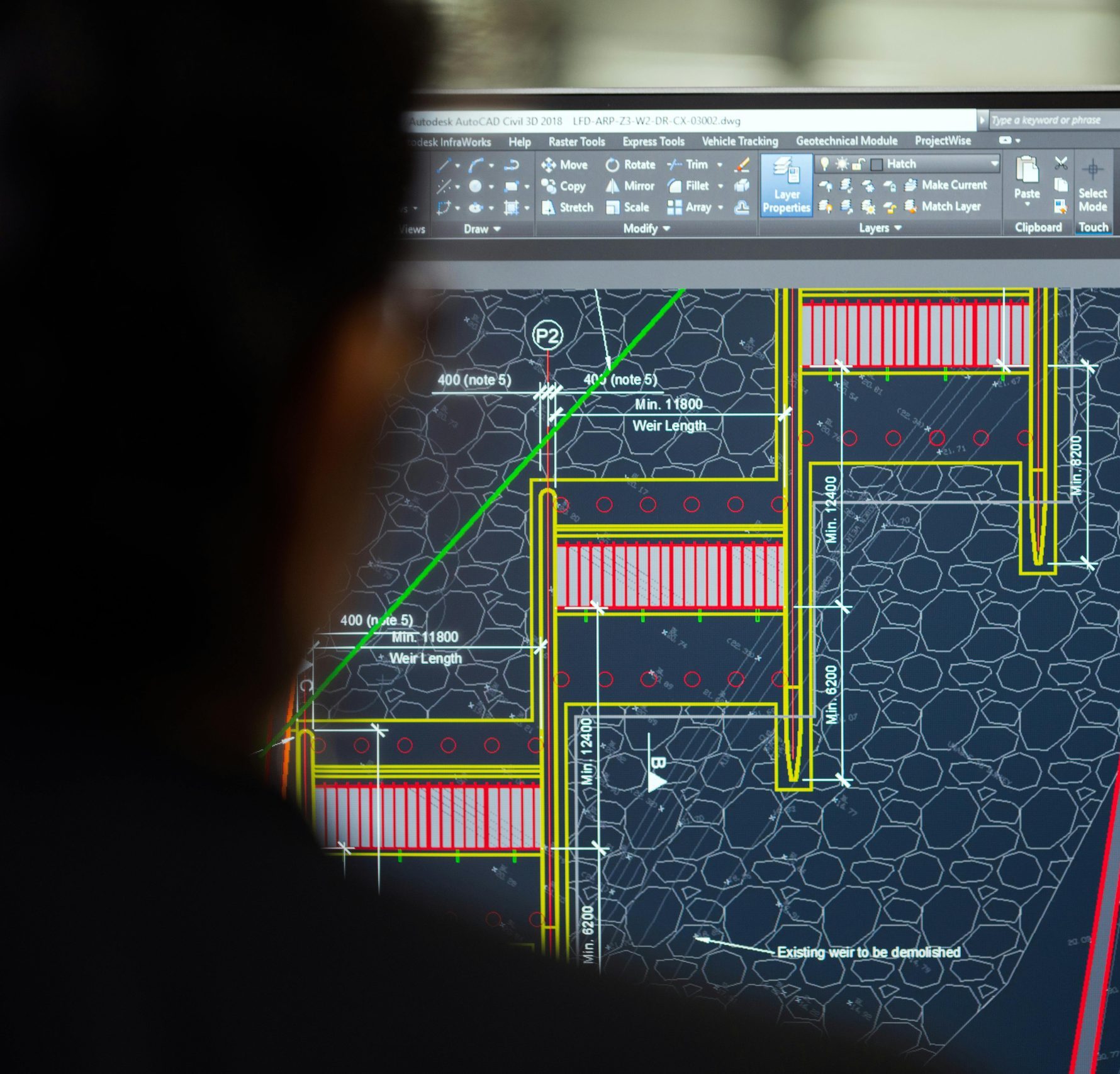 A civil engineer working on a weir design using CAD software on a computer screen in an office setting.